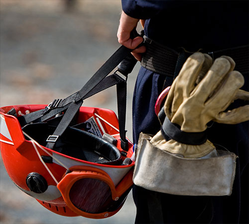 firefighter carrying protective fire retardant gear in side pocket while holding fireproof helmet and goggles